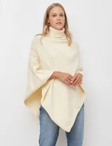 Poncho tejido color crema, con cuello polera y diseño trenzado diagonal en el frente. Presenta un corte asimétrico en el ruedo.