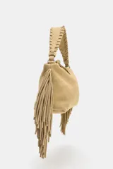 Bolso mini bandolera color beige de piel serraje con flecos en los laterales. Tiene asa de mano trenzada y asa bandolera extraíble.