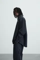 Camisa negra con finas rayas verticales blancas, de corte holgado, manga larga y cuello abotonado.