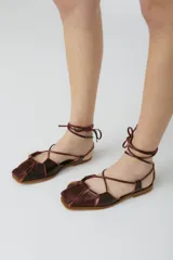 Sandalias bajas de cuero color marrón con tiras finas que se atan al tobillo.