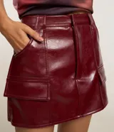 Short pollera de cuero sintético color bordó, con bolsillos delanteros con solapa y cierre frontal con cremallera.