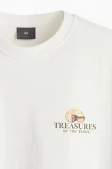 Remera blanca de algodón con cuello redondo y estampado pequeño en el pecho con la frase "Treasures of the Tides" y un dibujo de una concha. Corte holgado.