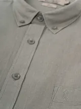 Camisa de manga larga azul, de lino y poliéster, con cuello abotonado y bolsillo en el pecho.