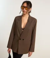 Blazer marrón de poliéster y viscosa, de corte amplio y estructura de sastrería, con solapas en el cuello, doble abotonadura, bolsillos falsos y pinzas.
