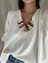 Collar con cuentas de cerámica, medallones grandes de resina color crema y detalles en rojo. Tiene tiento sintético con nudo corredizo para ajustar el largo.