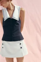 Falda pantalón corta de tiro alto color blanco con detalle de doble fila de botones negros en el frente y cierre lateral con cremallera oculta.
