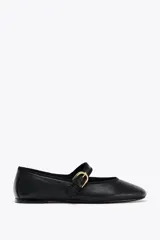 Zapato plano tipo bailarina color negro, confeccionado en piel, con tira sobre el empeine y hebilla metálica dorada ajustable. Tiene punta redonda y suela de 1.5 cm de altura.
