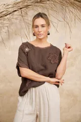 Blusa marrón de lino con escote redondo, mangas cortas con dobladillo y apliques florales en el frente.
