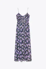 Vestido largo negro con estampado floral en tonos lila y verde. Escote en pico, tirantes finos, detalle drapeado en el busto, forro interior y cierre lateral con cremallera oculta.