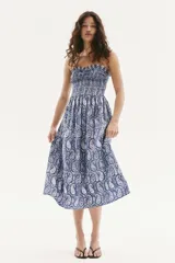Vestido midi de algodón con estampado paisley en tonos azules y blancos. Tiene breteles finos ajustables y escote recto con frunces. El cuerpo es fruncido con costura elástica en el busto y la falda tiene un leve vuelo.