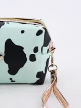 Neceser rectangular con estampado de manchas de vaca en tonos rosa y negro, cierre superior con cremallera dorada y correa de muñeca extraíble.