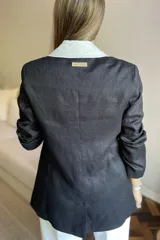 Blazer de lino color blanco con solapas y cuello en color beige, corte entallado, botón de nácar, tajo en la espalda y bolsillos laterales.