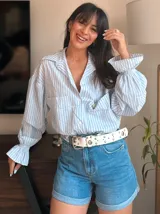 Camisa celeste y blanca a rayas verticales, con cuello clásico, cierre frontal con botones, mangas largas abullonadas con puños elásticos y dos bolsillos frontales.