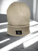 Gorro beanie de lana color beige con etiqueta negra con el logo de la marca Alquimia.