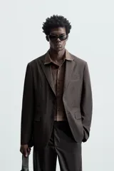 Blazer negro de corte relaxed fit, confeccionado en tejido de algodón con acabado ligeramente encerado. Tiene cuello con solapas de muesca, manga larga con puños abotonados, bolsillo de vivo en el pecho, bolsillos de solapa en la cadera, bolsillo interior, aberturas en la espalda y cierre frontal con botones.