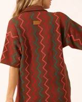 Vestido corto marrón con diseño de zig zag en verde y naranja, cuello tipo polo y cierre delantero con botones.