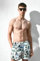 Short de baño blanco con estampado de palmeras, personas y paisajes en tonos azul, verde y rosa. Tiene cintura elástica con cordón ajustable, bolsillos laterales, bolsillo trasero con velcro y suspensor interior de malla.