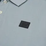 Remera tipo polo color petróleo con cuello de punto acanalado, puños de manga de punto plano y parche de silicona con el logo de Cat en el lado izquierdo del pecho.