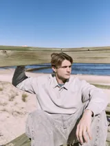 Polo de manga larga gris claro con cuello tipo camisa y cierre parcial con botones. Corte holgado y puños de canalé.