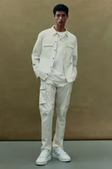 Sobrecamisa color crema con cuello inglés, cierre frontal con botones a presión, dos bolsillos superiores con solapa y puños ajustables con botón a presión.