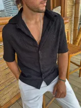 Camisa negra tejida de manga corta con cuello camisero y cierre frontal con botones.