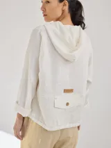 Chaqueta color beige de lino, con capucha, cierre frontal con cremallera negra, bolsillos laterales y mangas 3/4.