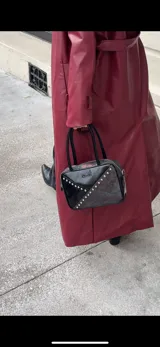 Cartera rígida negra de cuero con tachas plateadas y tres combinaciones de cuero diferentes que aportan textura. Tiene herrajes y cierre metálico plateado marca YKK. Cuenta con un asa fina para llevar al hombro o en la mano y una correa larga extra regulable.