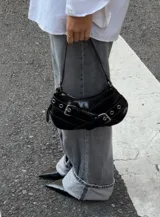 Cartera tipo baguette negra de cuero sintético con correa corta y detalles de hebillas plateadas.