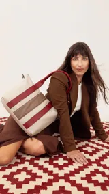 Cartera de mano color beige con divisiones y detalles en marrón y blanco. Tiene correa corta, correa larga ajustable, bolsillo trasero y bolsillos internos.
