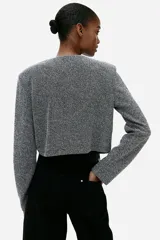 Saco corto de punto color gris jaspeado, con cuello redondo, cierre frontal con botones metálicos y bolsillos de parche decorativos.