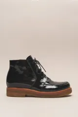 Bota de cuero vacuno con acabado charol, color marrón oscuro. Presenta un diseño de caña corta con cordones frontales y costuras decorativas en la puntera. La suela es de goma tipo crepe.
