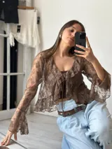Blusa marrón de encaje con volados, mangas acampanadas y lazo en el escote.