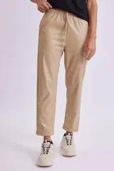 Pantalón de cuero sintético color beige con cintura elástica y cordón ajustable.