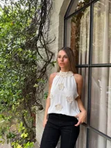 Blusa blanca sin mangas con cuello halter y apliques de flores de crochet.