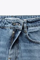 Pantalón de jean color crudo, de tiro alto, corte recto y largo tobillero. Tiene cinco bolsillos, cierre frontal con cremallera y botón metálico.