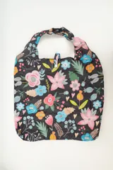 Tote bag de tela negra con estampado de flores y hojas en tonos rosa, celeste, naranja y verde.