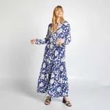 Vestido largo azul con estampado floral blanco, cuello panadero con lazo, mangas largas y corte escalonado.