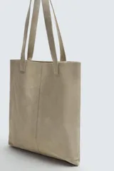 Bolso tipo shopper fabricado en piel con acabado serraje color gris oscuro. Tiene compartimento principal abierto con un bolsillo interior con cierre. Cuenta con dos asas de mano fabricadas en piel.