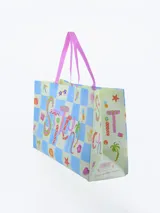 Bolsa de compras laminada con diseño estampado de Stitch en la playa, sobre un fondo a cuadros con motivos veraniegos.