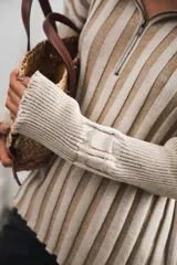 Buzo color beige con rayas horizontales en lurex dorado, cuello con medio cierre, corte oversized y logo tejido en el puño.