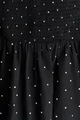 Vestido corto negro con lunares blancos, escote en V pronunciado, sección cut-out con detalle girado en el busto, espalda escotada fruncida, cierre oculto en un lateral y manga abullonada al codo con elástico fino en los puños.