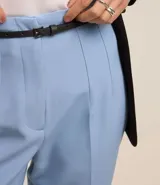 Pantalón de vestir rojo, estilo carrot (holgado en cadera y ajustado en tobillo), con pliegues frontales y cinturón de material sintético negro con hebilla pequeña.