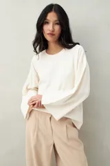 Sweater color beige de tejido de punto, con cuello redondo y mangas largas acampanadas con botones decorativos en los laterales.