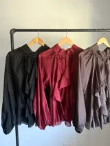 Camisa blanca de algodón italiano con cuello alto ajustable mediante lazo trasero, mangas abullonadas y un gran shabot frontal con volados en cascada.