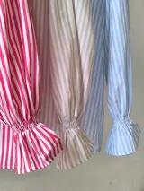 Camisa de mangas largas abullonadas, con puños elásticos y estampado a rayas verticales rojas y blancas.