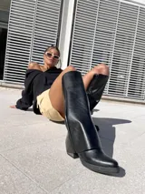 Botas negras de ecocuero, estilo texanas, de caña alta y taco cuadrado.