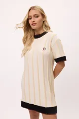 Vestido de tejido de punto color amarillo con rayas verticales en tono más claro. Presenta cuello redondo y puños en color celeste con terminación de pespunte en color naranja. Lleva un bordado de iniciales en el pecho.