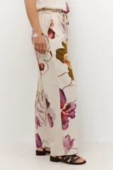 Pantalón de lino color celeste con estampado de flores grandes en tonos marrones, azules y rojos. El pantalón es de corte ancho y tiene cintura alta con cordón ajustable.