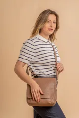 Bandolera de hombro color gris claro, con solapa frontal y correa ajustable. Presenta un diseño simple y práctico, ideal para uso diario.