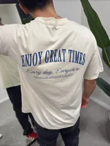Remera beige de algodón con estampado en la espalda que dice "ENJOY GREAT TIMES Every day. Everywhere EMBRACE THE DIFFERENCE WORLDWIDE".